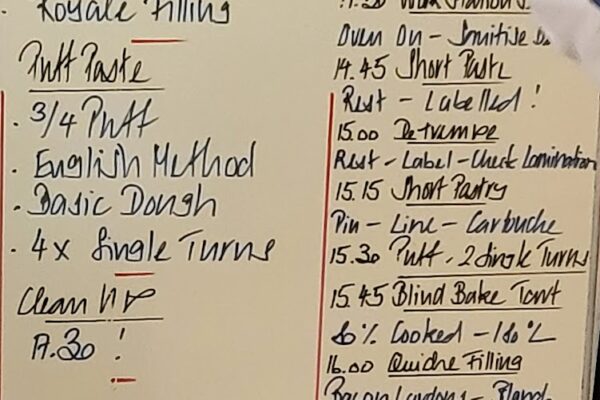 Chef Mario's hand writing on the board during basic course